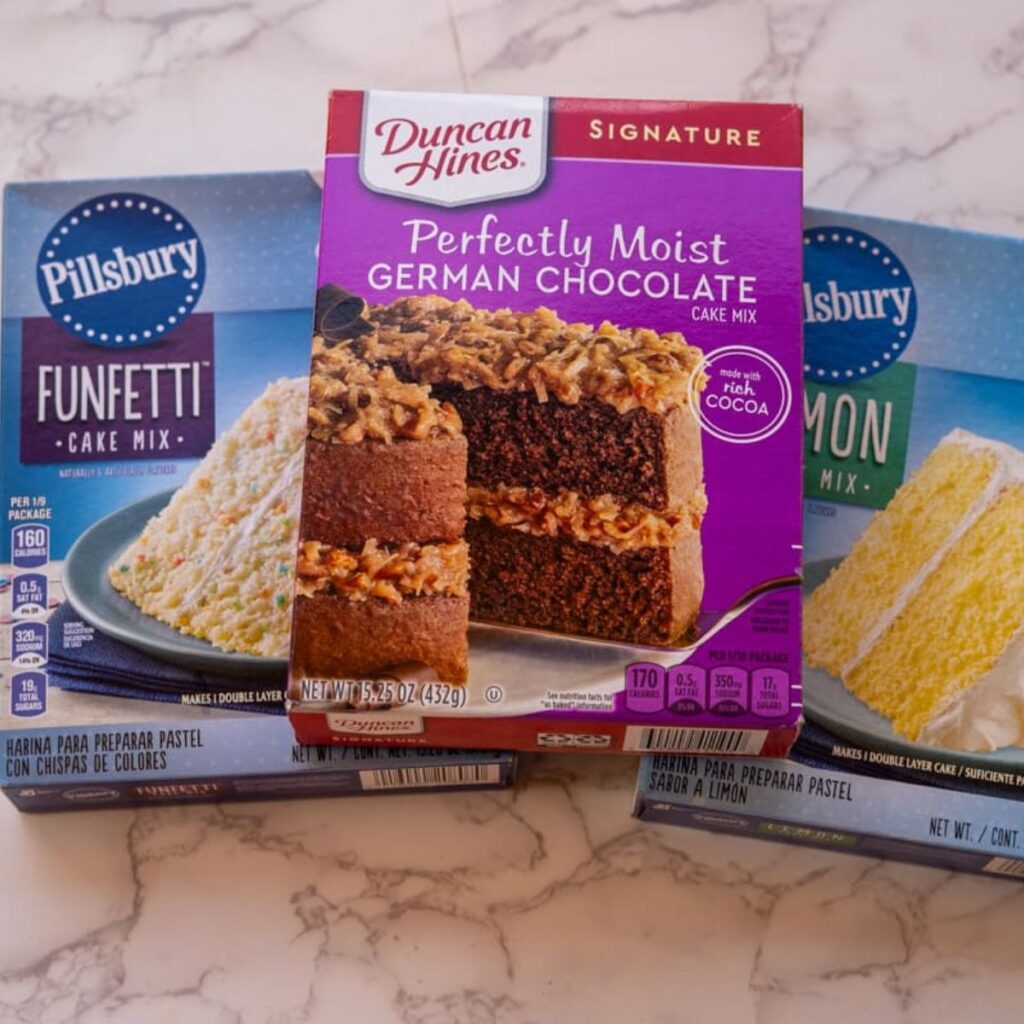 Boxes of cake mix on a marble surface: Pillsbury Funfetti, Duncan Hines German Chocolate, and Pillsbury Lemon—perfect for making a quick and delightful mug cake from box mix.