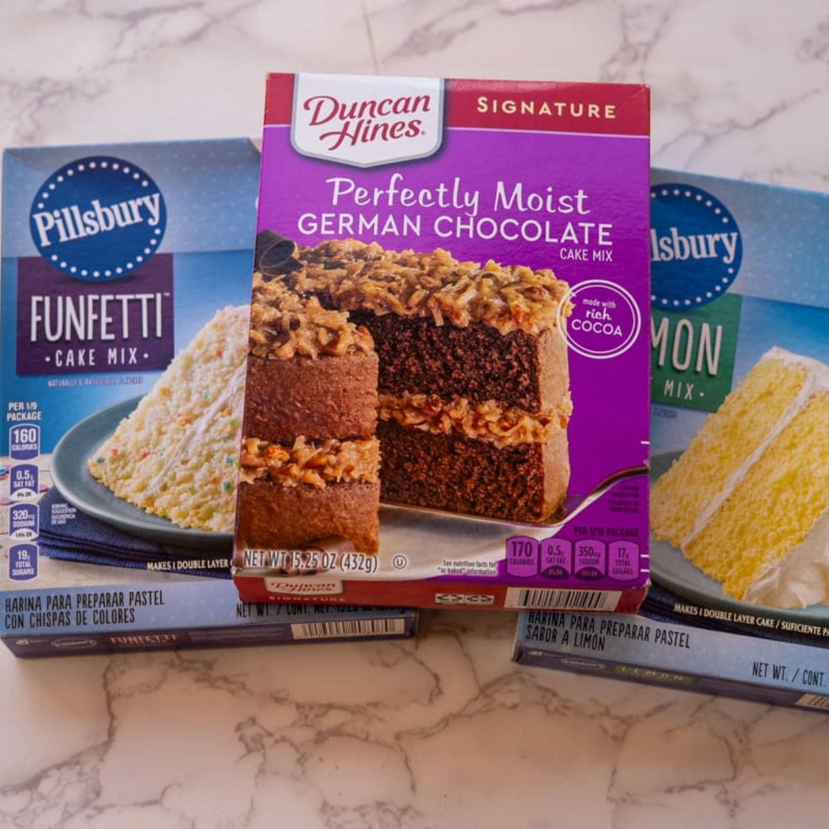 Boxes of cake mix on a marble surface: Pillsbury Funfetti, Duncan Hines German Chocolate, and Pillsbury Lemon—perfect for making a quick and delightful mug cake from box mix.