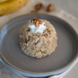 A scoop of banana walnut mug cake topped with whipped cream and a walnut half, served on a gray ceramic plate.