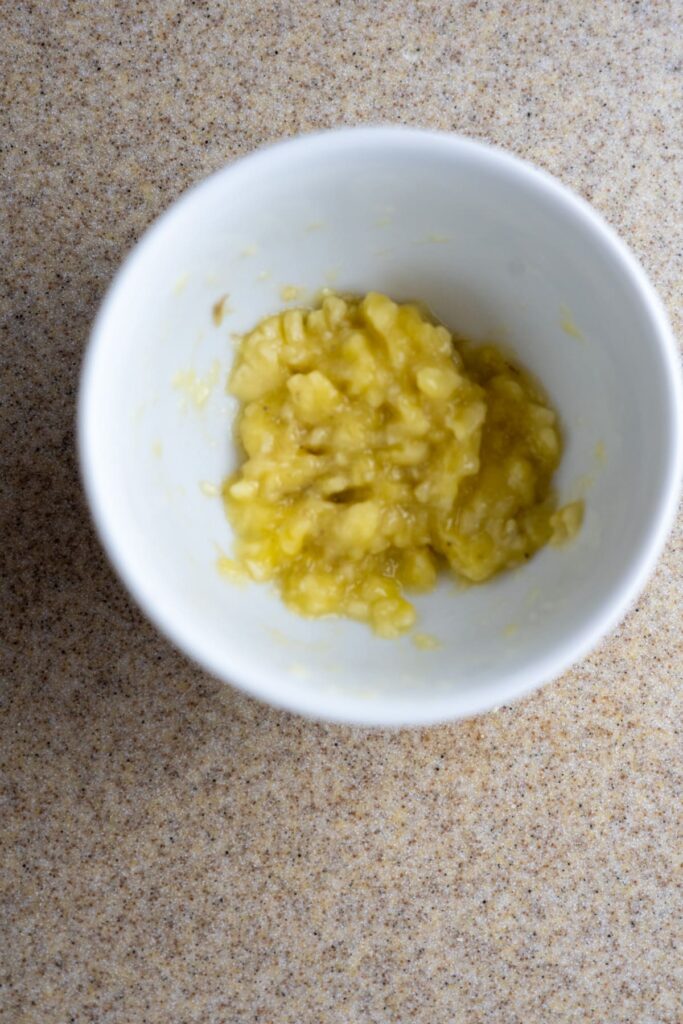 A white bowl containing mashed banana sits on a speckled countertop.