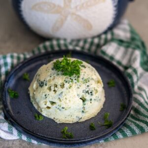 A serving of steamed egg and spinach dish garnished with fresh parsley, presented on a blue plate with a green checkered cloth underneath.