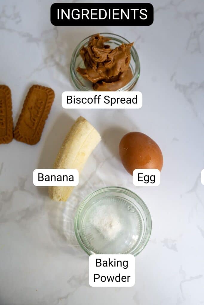 Top-down view of labeled ingredients on a white surface: Biscoff spread, banana, egg, baking powder, and two Biscoff cookies.
