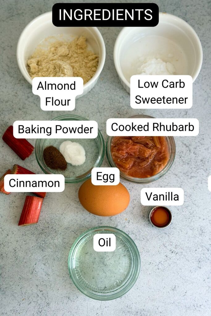 Seven labeled ingredients for a recipe: almond flour, low carb sweetener, baking powder, cooked rhubarb, cinnamon, egg, vanilla, and oil, displayed on a light surface.