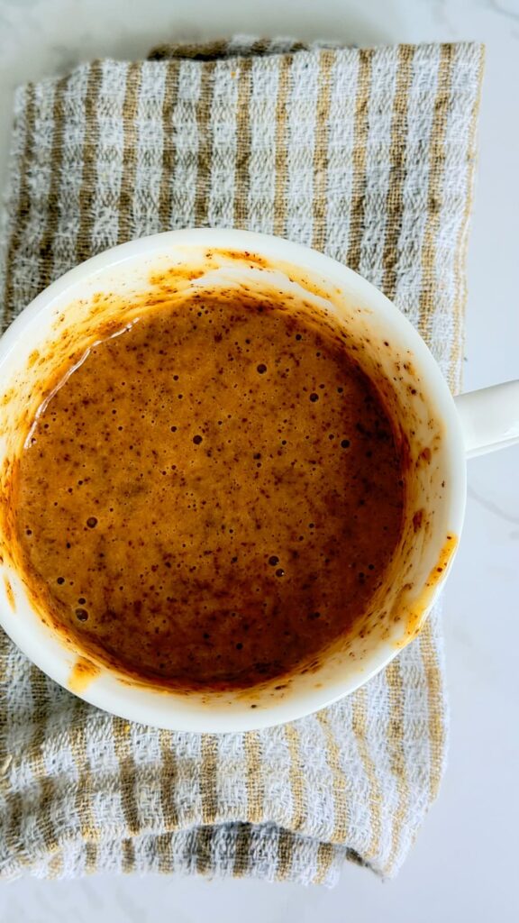 A white mug filled with an almond butter mug cake, resting on a striped cloth.