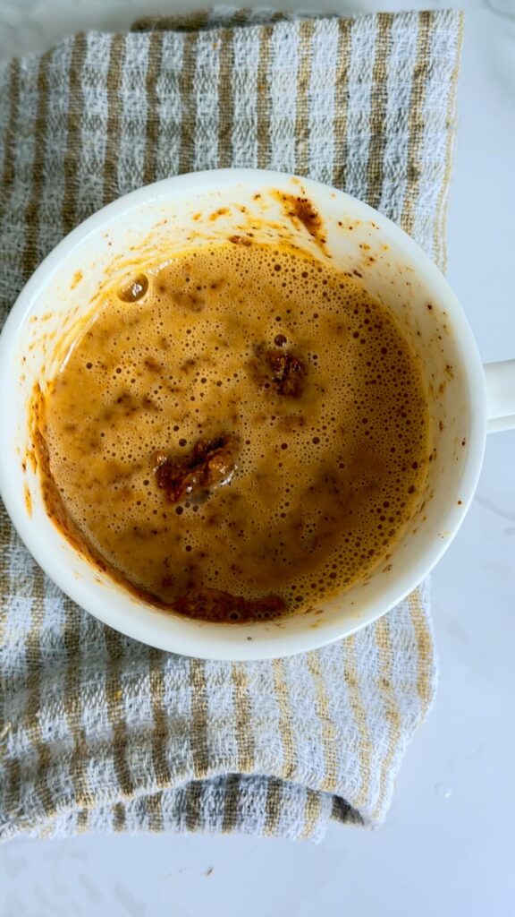 A white mug filled with a warm almond butter mug cake, sitting on a striped kitchen towel.